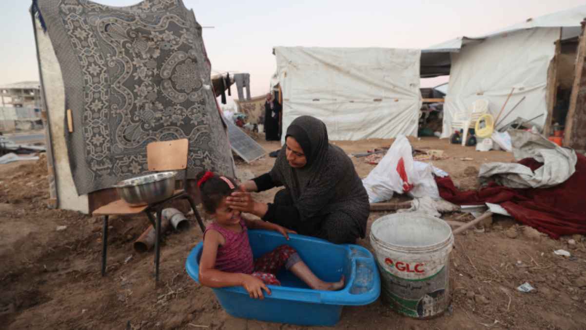 من بقايا البيت المهدّم.. أم تُعيد الحياة لطفلتها بالماء القليل